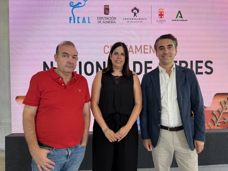 Tres personas de pie posan ante una pantalla rosa con logotipos y el texto Certamen Nacional de Series.