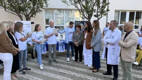 Un grupo de personas, algunas con camisetas reivindicativas y un sanitario con bata, posa junto a carteles en una plaza.