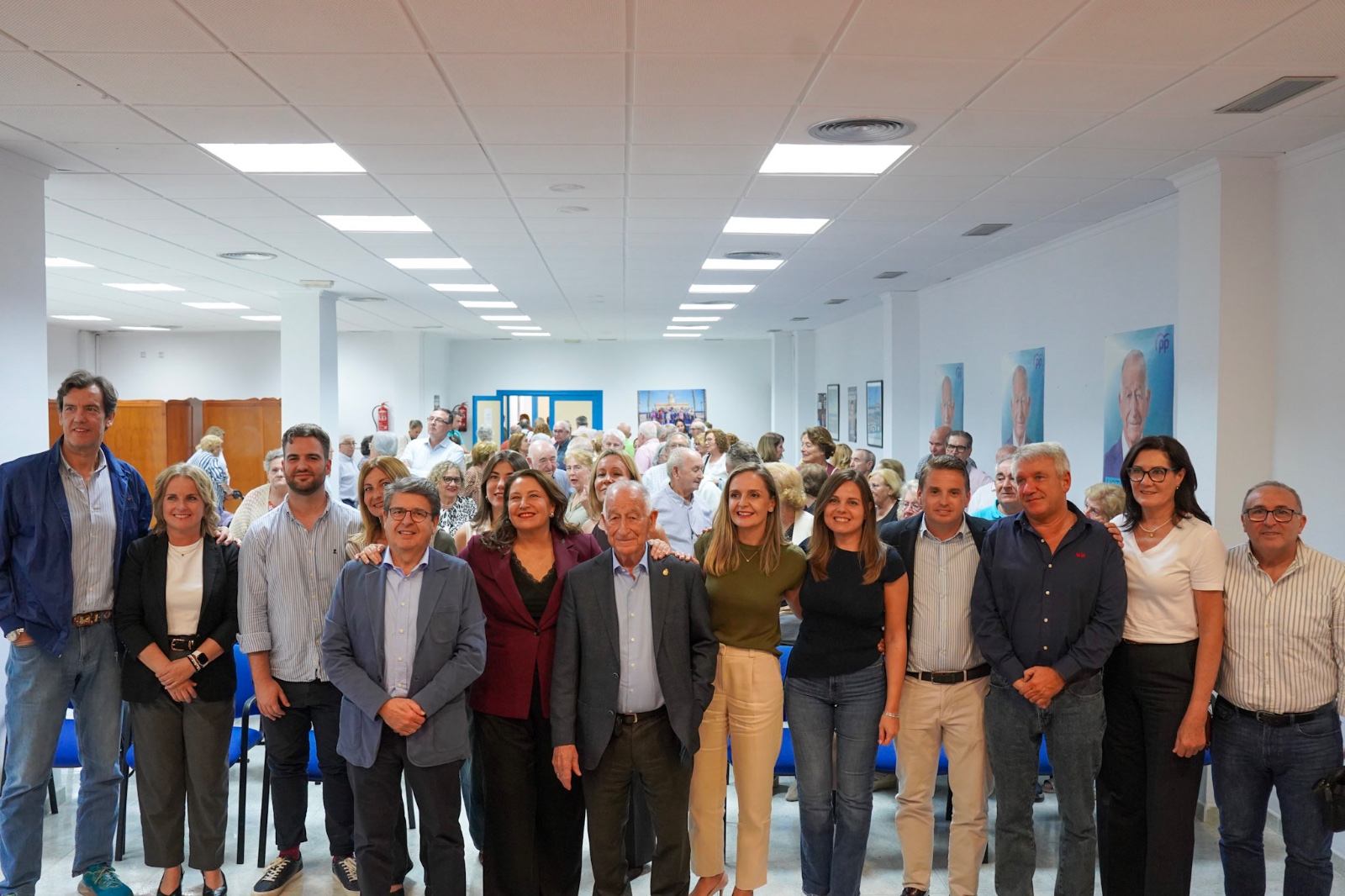 Un grupo numeroso de personas posa de pie en una sala amplia con carteles en las paredes.