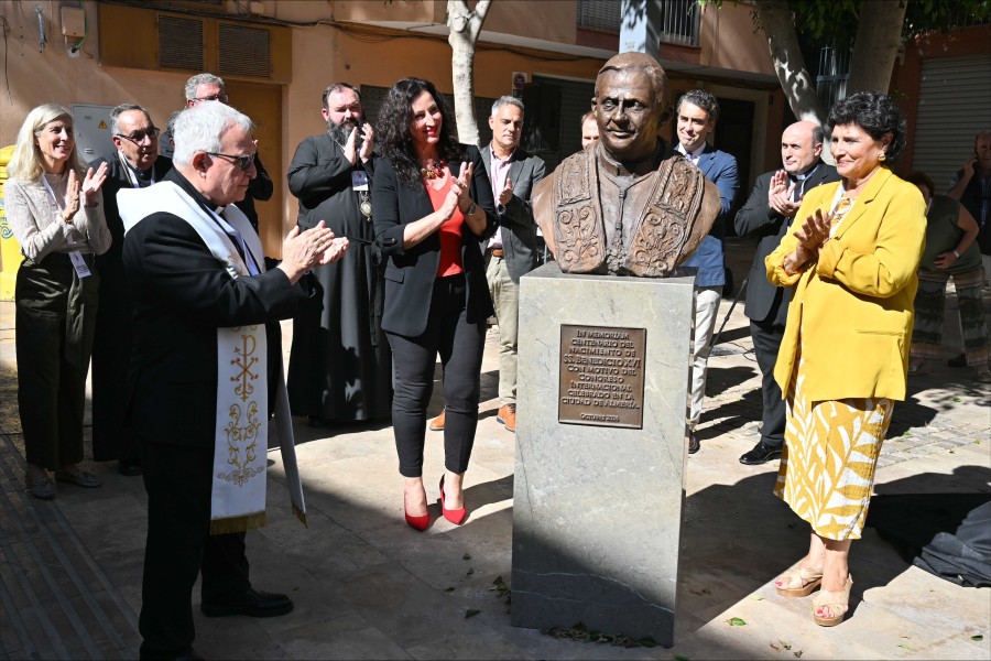 Un grupo de personas aplaude alrededor de un busto de bronce sobre un pedestal de piedra en una calle.
