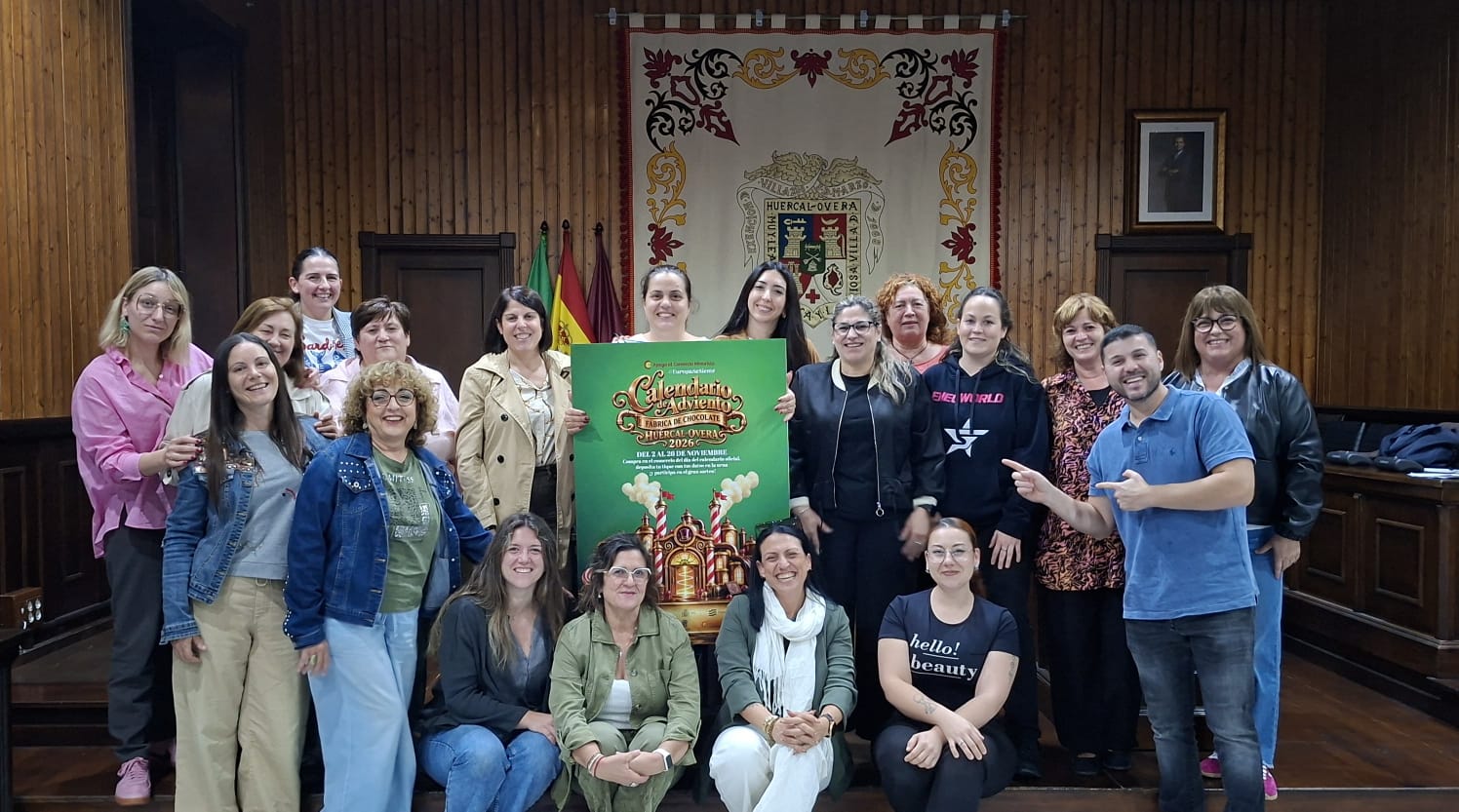 Un grupo de personas posa en una sala con paredes de madera junto a un cartel verde de un calendario de adviento.