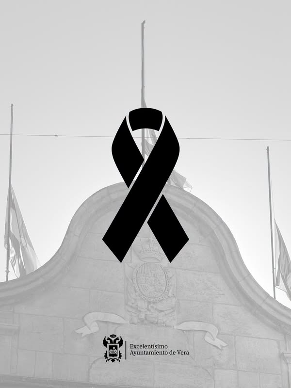 Un lazo negro sobre la fachada de piedra de un edificio con escudo y mástiles, en blanco y negro.