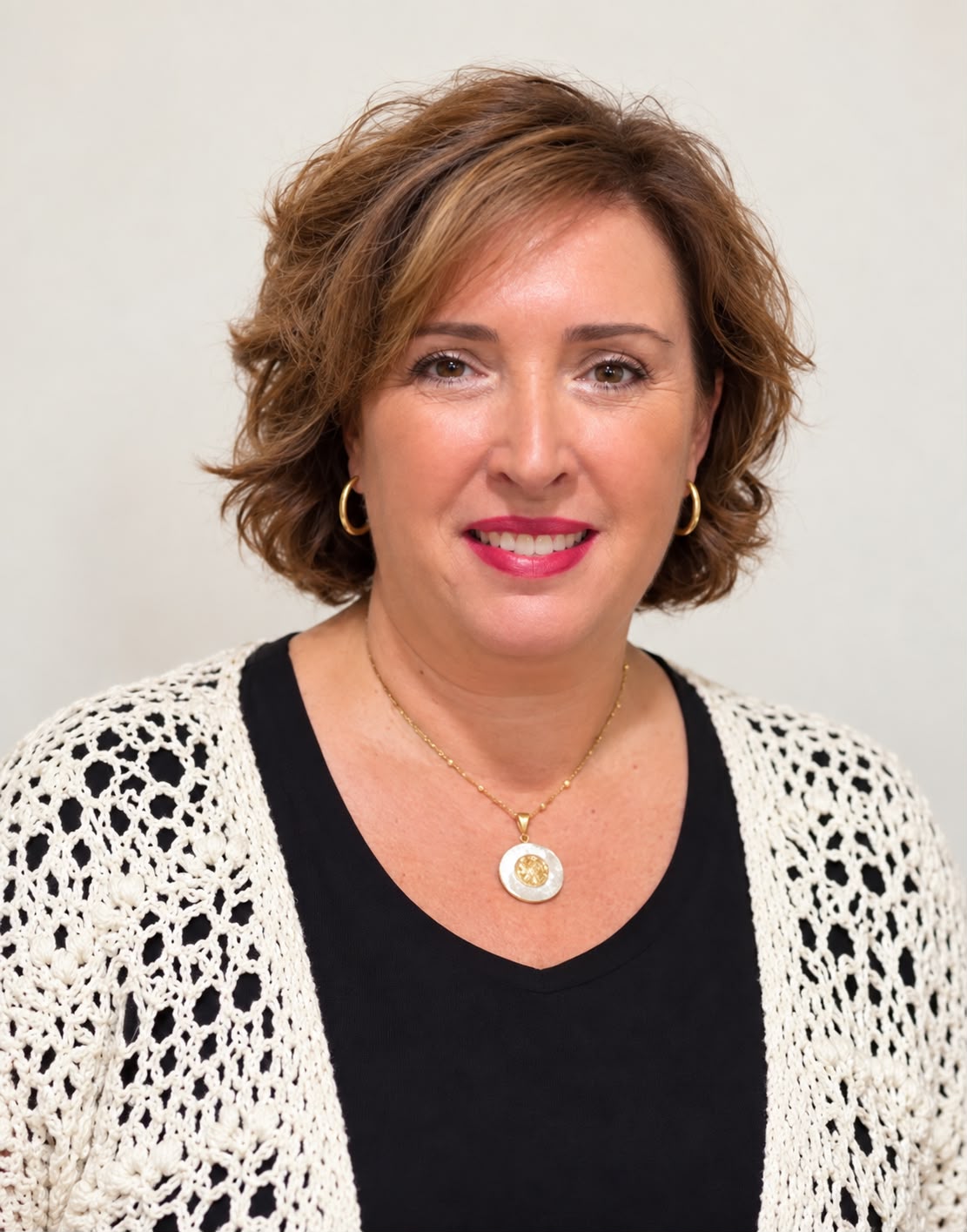 Retrato de una mujer sonriente de pelo castaño corto, labios rojos y rebeca calada blanca sobre fondo claro.