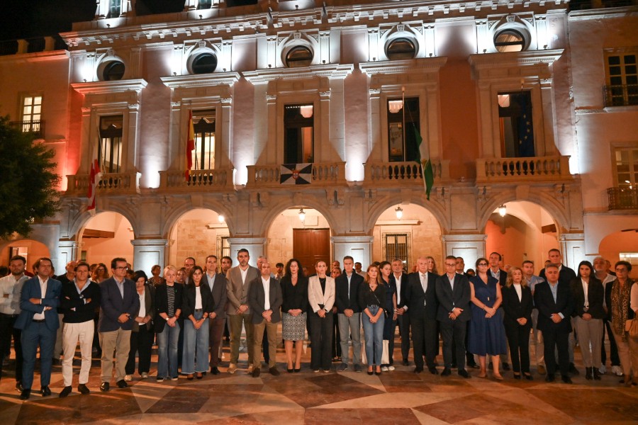 Un grupo numeroso de personas vestidas de luto posa de noche ante la fachada iluminada de un edificio con arcos y balcones.