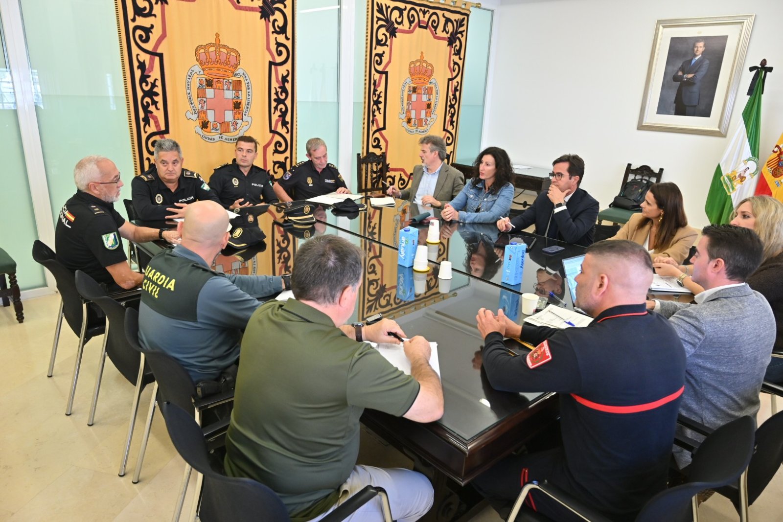 Un grupo de personas, varias con uniforme policial, sentadas alrededor de una mesa de reuniones en una sala con banderas y escudos.