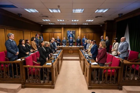 Un grupo de personas trajeadas de pie en una sala de reuniones con mesas de madera y sillas rojas.